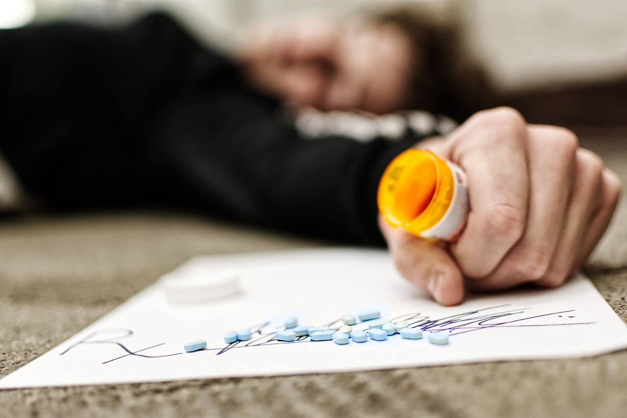 Person suffering from substance abuse holding an open pill bottle, highlighting the dangers of drug addiction.